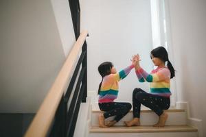 Sibling Asian girls playing rock paper scissors hand game. children sitting on stairs at home playing together. photo