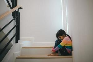 triste niño desde esta padre y madre discutiendo, familia negativo concepto. pequeño muchachas sentado y llorando a el escaleras. foto