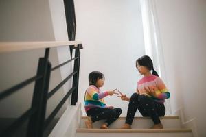 Sibling Asian girls playing rock paper scissors hand game. children sitting on stairs at home playing together. photo