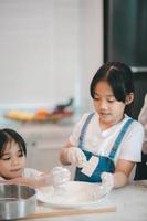Two little cute Asian girls, learning how to make bread and bakery with a curious and happy smile face. She learns and plays photo
