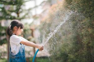 Asian little child girl water the plants. kid helps to care for the plants in the garden. photo