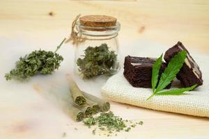 Pre-Roll cannabis joints and cake brownies with cannabis buds in a clear glass jar laying on the sackcloth photo