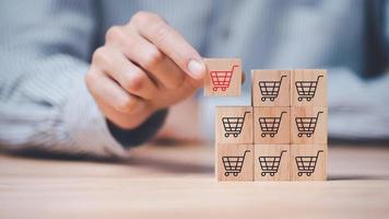 Wooden block in businessman hand ,shopping cart icon,Consumer society ,Shopping service on online web and offers home delivery ,online shopping or e-shopping ,Shop online with a smartphone app