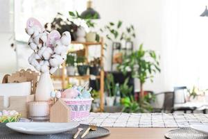 Easter decoration of colorful eggs in a basket and a rabbit on the kitchen table in a rustic style. Festive interior of a country house photo