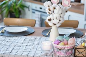 Easter decoration of colorful eggs in a basket and a rabbit on the kitchen table in a rustic style. Festive interior of a country house photo