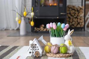 Key to house near fireplace stove with fire and firewood. Cozy home hearth with easter decor, colorful eggs in a basket and bunny. Building, moving, mortgage, rent and purchase real estate, insurance photo