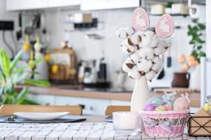 Easter decoration of colorful eggs in a basket and a rabbit on the kitchen table in a rustic style. Festive interior of a country house photo