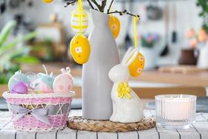 Easter decoration of colorful eggs in a basket and a rabbit on the kitchen table in a rustic style. Festive interior of a country house photo