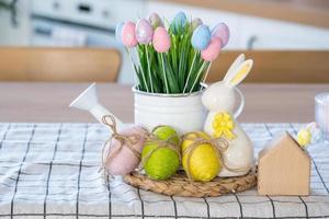 Easter decoration of colorful eggs in a basket and a rabbit on the kitchen table in a rustic style. Festive interior of a country house photo