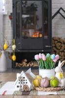 Key to house near fireplace stove with fire and firewood. Cozy home hearth with easter decor, colorful eggs in a basket and bunny. Building, moving, mortgage, rent and purchase real estate, insurance photo