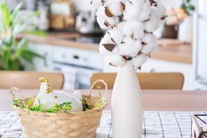 Easter decoration of colorful eggs in a basket and a chicken on the kitchen table in a rustic style. Festive interior of a country house photo