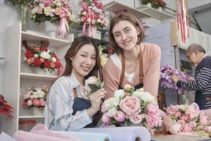 Two Young beautiful female florist partners arranging and decorating bunch of blossoms together smile with happy work in colorful flower shop store with fresh blooms, small business SME entrepreneur. photo