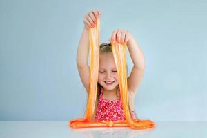 Cute funny girl play with orange slime. Kid squeeze and stretching toy slime. photo