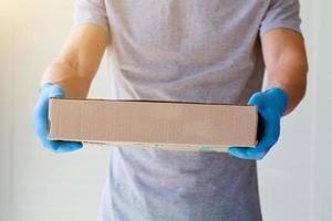 A courier in rubber blue gloves holds out a cardboard box. Fast and free Delivery transport. photo