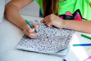 Close-up of girls hands draw with crayons in antistress coloring. photo
