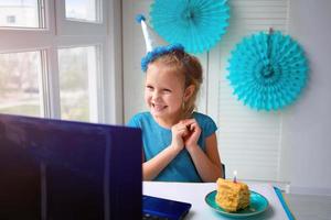 contento chica, vistiendo un azul vestir y un gorra ese celebra cumpleaños vía el Internet en cuarentena tiempo, autoaislamiento y familia valores, en línea cumpleaños. foto