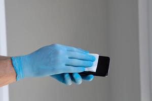 cerca arriba es para hombres es manos en médico caucho guantes a frotar un móvil teléfono pantalla con un servilleta. foto