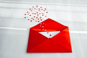 Opened red envelope and many felt hearts on white background with place for text. Love letter mail correspondence relationship. Valentines day concept. Top view. photo