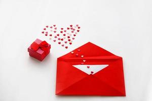 Opened red envelope and many felt hearts and a box with a gift on white background with place for text. Love letter mail correspondence relationship. Valentines day concept. Top view. photo