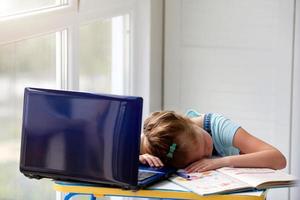 cansado niña Chica de escuela mentiras en cuadernos en frente de un ordenador portátil. distancia aprendiendo. foto