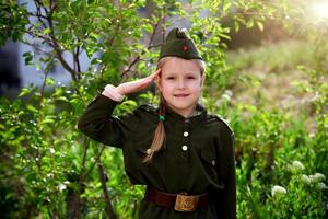 retrato contento niña en uniforme poner un mano a su cabeza en un verde antecedentes. victoria día. foto