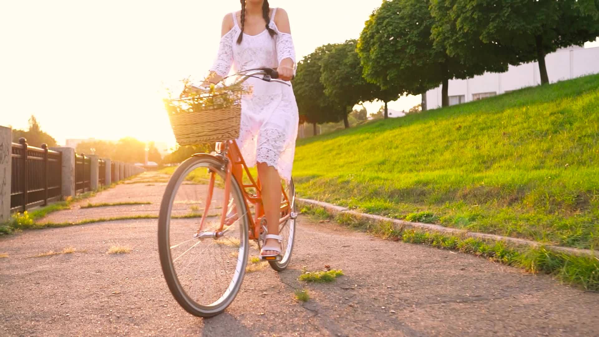 Young beautiful woman sitting on her bicycle with flowers at sunset ...