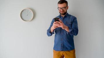 Bearded man using smartphone against a gray wall with a clock