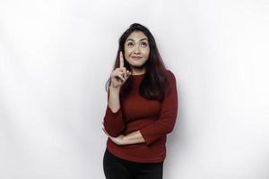 Excited Asian woman dressed in red, pointing at the copy space on top of her, isolated by white background photo