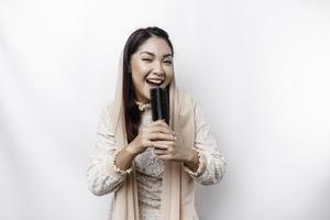 Portrait of carefree Asian Muslim woman, having fun karaoke, singing in microphone while standing over white background photo