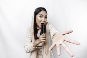 Portrait of carefree Asian Muslim woman, having fun karaoke, singing in microphone while standing over white background photo
