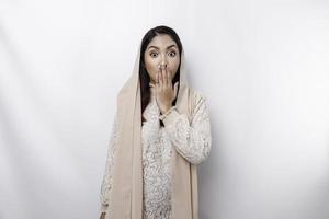 Oops Surprised young Asian Muslim woman covering mouth with hands and staring at camera while standing against white background photo