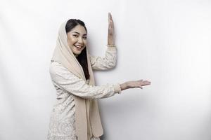 Young Asian Muslim woman smiling while pointing to copy space beside her photo