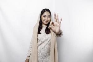 Portrait of a smiling Asian Muslim woman, giving an OK hand gesture isolated over white background photo