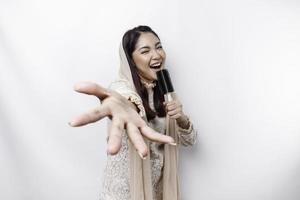 Portrait of carefree Asian Muslim woman, having fun karaoke, singing in microphone while standing over white background photo