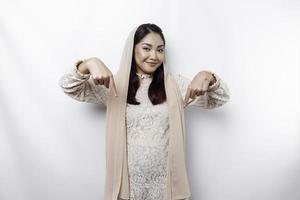 Excited Asian Muslim woman hijab pointing at the copy space below her, isolated by white background photo