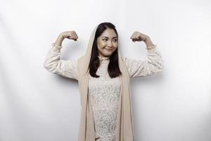 Excited Asian Muslim woman wearing a headscarf showing strong gesture by lifting her arms and muscles smiling proudly photo