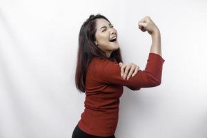 emocionado asiático mujer vistiendo un rojo parte superior demostración fuerte gesto por levantamiento su brazos y músculos sonriente con orgullo foto