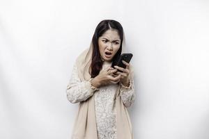 A depresses Asian Muslim woman wearing a headscarf looks stressed while talking on the phone isolated by white background photo