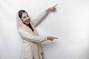 Young Asian Muslim woman smiling while pointing to copy space beside her photo