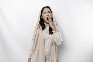 Portrait of sleepy attractive Asian Muslim woman wearing a headscarf, feeling tired after night without sleep, yawning, covering opened mouth with palm photo