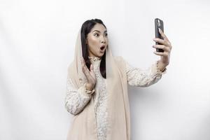 conmocionado asiático mujer vistiendo Pañuelo, participación su teléfono, aislado por blanco antecedentes foto