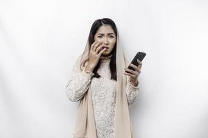 A depresses Asian Muslim woman wearing a headscarf looks stressed while talking on the phone isolated by white background photo