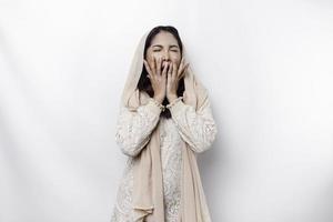 Portrait of sleepy attractive Asian Muslim woman wearing a headscarf, feeling tired after night without sleep, yawning, covering opened mouth with palm photo