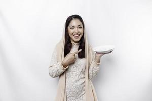 An Asian Muslim woman is fasting and hungry and holding utensils cutlery while looking aside thinking about what to eat photo