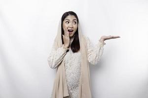 Shocked Asian Muslim woman pointing at the copy space on beside her, isolated by white background photo