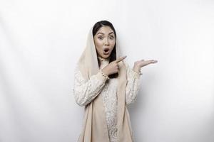 conmocionado asiático musulmán mujer señalando a el Copiar espacio en junto a su, aislado por blanco antecedentes foto