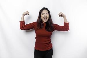 emocionado asiático mujer vistiendo un rojo parte superior demostración fuerte gesto por levantamiento su brazos y músculos sonriente con orgullo foto