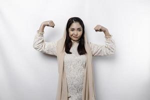 Excited Asian Muslim woman wearing a headscarf showing strong gesture by lifting her arms and muscles smiling proudly photo