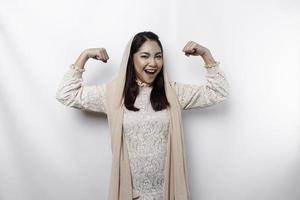 Excited Asian Muslim woman wearing a headscarf showing strong gesture by lifting her arms and muscles smiling proudly photo