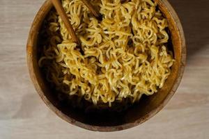 Fried instant noodles with chopsticks on a wooden bowl and wooden table photo